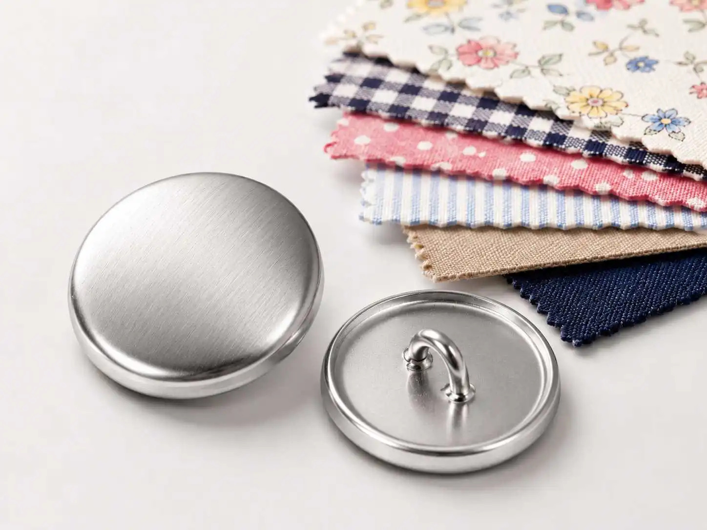 making fabric covered buttons, Metal button shells and shank backs are displayed beside patterned fabric samples for making fabric covered buttons.